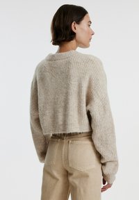 Gebreide trui in lichtbeige met een geribbelde textuur, cropped design en verlaagde schouders, gecombineerd met lichtbeige high-waisted jeans.