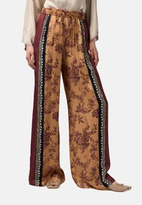 Wijdvallende bloemenbroek in mosterd met bordeauxrode en zwarte zijkanten. Bevat een koordsluiting aan de taille en een bloemendessin door het geheel.