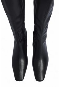 Čierne kožené čižmy po kolená s špicatou špičkou, hladkým povrchom a prešívaním pozdĺž šachty.