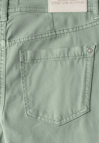 Svetle zelená denimová tkanina s zadní kapsou s vyšitým obrysem a stříbrným knoflíkovým akcentem. Viditelná nášivka "STREET ONE".