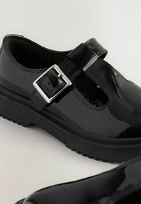 Chaussures en cuir verni noir avec un bout fermé, des côtés découpés et un détail de boucle en argent. Semelle en caoutchouc épaisse avec un motif texturé.
