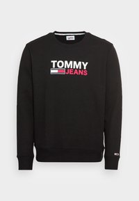 Sudadera negra con cuello redondo y puños acanalados, con un audaz logo "TOMMY JEANS" en blanco y rosa en el frontal.
