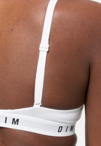 Primo piano della schiena di una persona che indossa un reggiseno bianco con spalline regolabili, con la scritta "DIM" stampata in nero sul bordo.