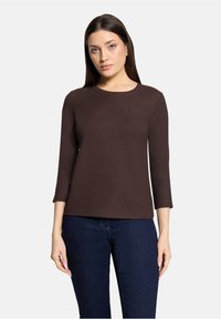 Braunes, strukturiertes Oberteil mit dreiviertel Ärmeln, rundem Ausschnitt und figurbetontem Schnitt. Kombiniert mit dunkelblauen Jeans. Weiches Material.