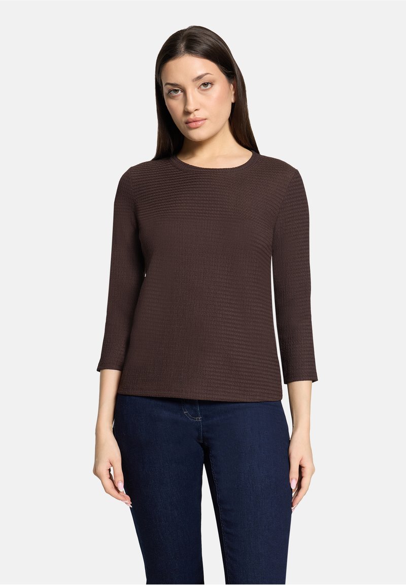 Braunes, strukturiertes Oberteil mit dreiviertel Ärmeln, rundem Ausschnitt und figurbetontem Schnitt. Kombiniert mit dunkelblauen Jeans. Weiches Material.