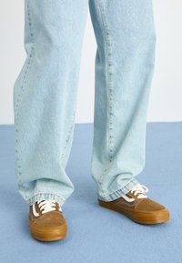 Hnědé semišové tenisky s bílými akcenty, gumovými podrážkami a bílými tkaničkami; doplněné o světle modré, mírně volné džíny.