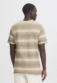 T-skjorte med kortermet og horisontale striper i Beige og dempet brunt. Laget av lett stoff med en teksturert overflate. Rund hals.