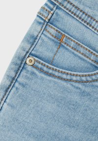 Jeans de mezclilla azul claro con costuras visibles en un color naranja contrastante, con bolsillos y un detalle de botón metálico de marca.