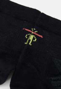 Schwarze Socken aus strukturiertem Stoff, mit einem grünen grafischen Design und einem roten Akzent. Musterdetails sind im oberen Abschnitt sichtbar.
