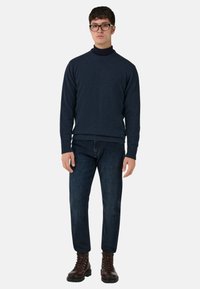 Granatowy dziany sweter z prążkowanym, okrągłym dekoltem, zestawiony z ciemnoniebieskimi dżinsami i brązowymi skórzanymi butami na sznurówki. Prosty, elegancki design.