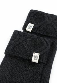 Schwarze gestrickte Socken mit einem strukturierten Muster, ausgestattet mit einem umgeschlagenen Bündchen und einem Etikett mit einem Schädel-Design. Weiches, warmes Material.