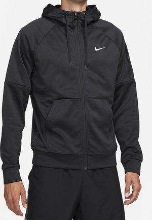 Mand iført sort Nike hættetrøje med lynlås, frontlomme og logo på brystet, kombineret med sorte bukser, vist fra nakke til hofter.