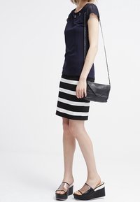 Marinebluse med blomsterudsmykninger, stribet sort-hvid nederdel, sort clutch-taske og platformsandaler med gennemsigtige stropper.