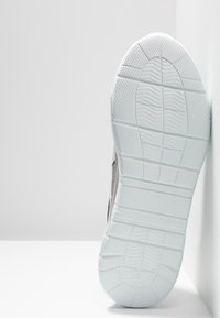 Semelle de chaussure de sport blanche avec surface en caoutchouc texturé, stries et rainures pour l'adhérence. La partie supérieure est en tissu gris clair avec une finition lisse.