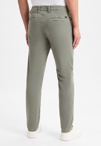 Lichtgroene katoenen chino's met een rechte pasvorm, voorzien van twee achterzakken en een tailleband, gecombineerd met witte schoenen.