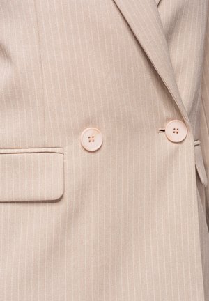 Blazer beige à fines rayures avec deux boutons rose clair et une poche à rabat sur le côté gauche.