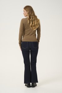 Bruine aangesloten trui met lange mouwen, gecombineerd met donkerblauwe flared jeans. Model getoond vanaf de achterkant, met krullend haar en zwarte schoenen.