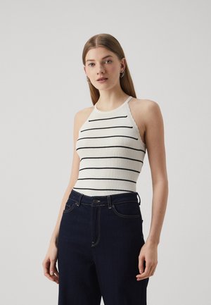 Haut halter blanc à rayures horizontales noires, associé à un jean taille haute bleu foncé avec de subtils détails de couture.