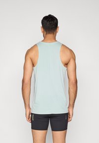 Šviesiai mėlynas marškinėliai be rankovių su apvalia iškirpte, pagaminti iš lygaus audinio, derinami su juodais šortais su logotipu.