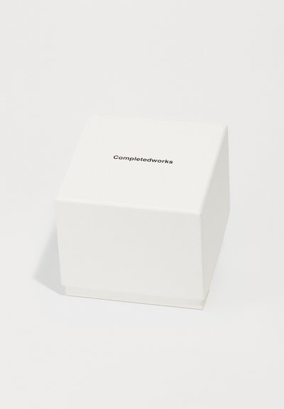 Weißer quadratischer Kasten aus strukturiertem Papier, mit dem gedruckten Text "Completedworks" in Schwarz auf der oberen Fläche.