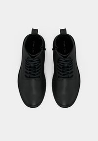 Bocanci negri din piele la gleznă, cu o textură netedă, sistem de închidere cu șireturi și o buclă de prindere la călcâi. Design minimalist și vârf rotunjit.