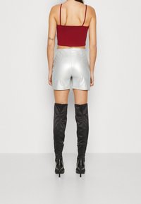 Top corto rojo, pantalones cortos plateados brillantes, botas negras por encima de la rodilla. Los pantalones cortos presentan una textura suave y un detalle lateral.