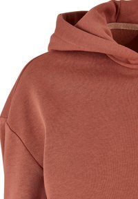 Felpa con cappuccio in un morbido colore ruggine testurizzato. Presenta una vestibilità morbida con scollo ampio e dettagli di cuciture visibili intorno al cappuccio.