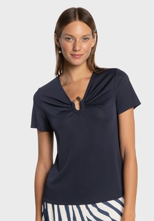 Short-sleeve navy top with a V-neck, featuring gathered fabric at the neckline and a circular keyhole detail with gold accents.