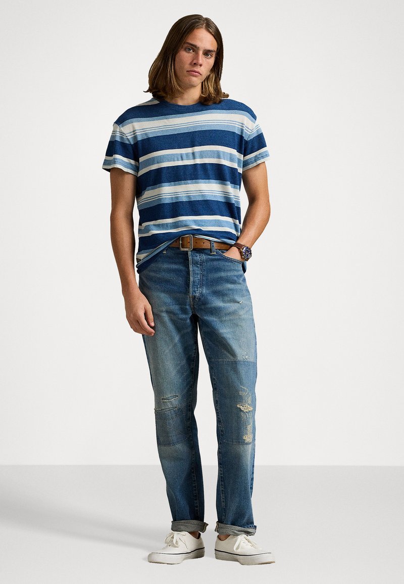 Gestreepte blauw-witte t-shirt, blauwe versleten jeans, bruine riem en witte schoenen. Casual outfit met een relaxte pasvorm en opgerolde mouwen.