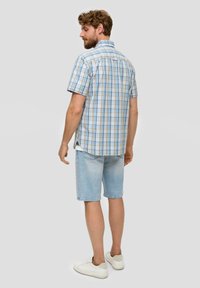 Korte mouwen geruit overhemd in blauw- en bruintinten, gecombineerd met lichte denimshorts en witte sneakers. De stof lijkt lichtgewicht en casual te zijn.