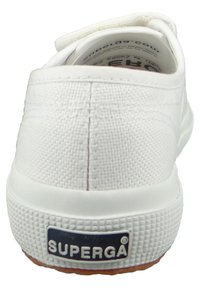 Sneaker bianco in tela con superiore testurizzato, suola in gomma e un'etichetta blu sul tallone. Il design è a bassa altezza con punta arrotondata.