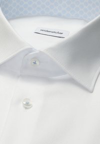 Col de chemise texturée blanche avec des boutons teintés de bleu et une étiquette « seidensticker » à l'intérieur de l'encolure.