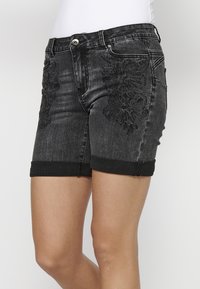 Črne jeans kratke hlače z vezenimi cvetličnimi vzorci na obeh straneh, s preklopnim robom in srebrnim gumbom na pasu.