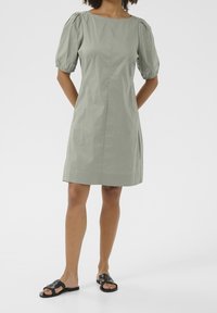 Klänning med puffärmar i ljusgrön bomull, med fyrkantig halsringning, enkla sömnadsdetaljer och rak silhuett. Matchas med svarta sandaler.