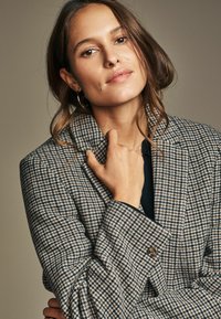 Karierter Blazer in Braun und Creme mit Reverskragen, Einzelknopfverschluss und taillierter Passform. Glatte Textur, leichter Glanz.