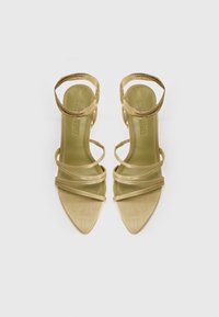 Sandales dorées à bride avec un petit talon, présentant un bout pointu et plusieurs fines lanières. Texture lisse avec une finition brillante.