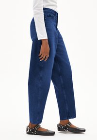 Hoge taille, wijde jeans in donkerblauwe denim met een zachte textuur. Gepaard met zwarte platte schoenen met studs.