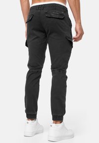 Pantalon cargo noir à coupe fuselée avec des poignets élastiques, doté de multiples poches et d'un tissu doux et texturé.