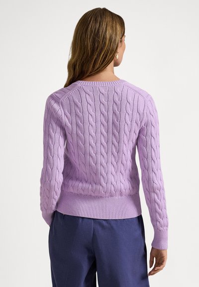 Μωβ πουλόβερ με πλέξη κόμπου, με ριμπ τελείωμα και μανίκια, διαθέτοντας κλασικό στρογγυλό λαιμό και υφή στο σχέδιο, φορεμένο πάνω από μπλε σκούρο παντελόνι.