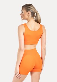 Oranje sportbeha en shorts met hoge taille, gemaakt van glad, rekbaar materiaal. Naadloos ontwerp, aansluitende pasvorm en minimalistische stijl.