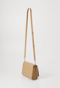 Beige rektangulær veske laget av teksturert materiale, med en lang justerbar stropp og gullhardware-detajer.