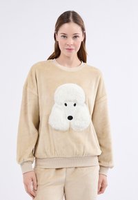 Beżowy pluszowy sweter z dużą aplikacją białego pudla, z okrągłymi uszami, czarnym nosem oraz ściągaczami przy mankietach i u dołu.