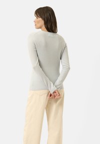 Helles blaues, figurbetontes Strickpullover mit langen Ärmeln, weicher Textur und Rundhalsausschnitt, kombiniert mit creamfarbenen, weit geschnittenen Hosen.