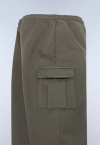 Grüne Sweatpants aus einem strukturierten Stoff, mit elastischem Bund und einer großen Seitentasche mit Klappe.