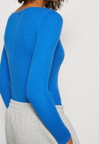 Long-sleeve ribbed top in vibrant blue color, made of a textured knit material. The neckline is slightly rounded, complemented by a plain design.
