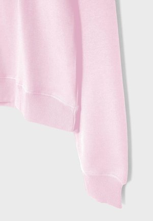 Lyserød sweatshirtærme med ribbet manchet og nederste kant på en ensformet lys baggrund.