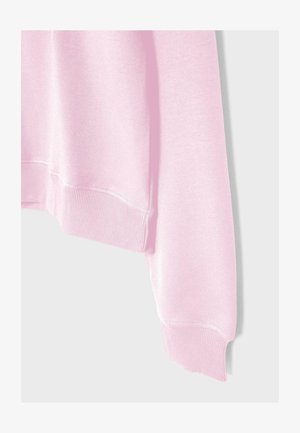 Světlounce růžový rukáv mikiny s žebrovaným lemem u manžety a spodního okraje na jednoduchém světlém pozadí.