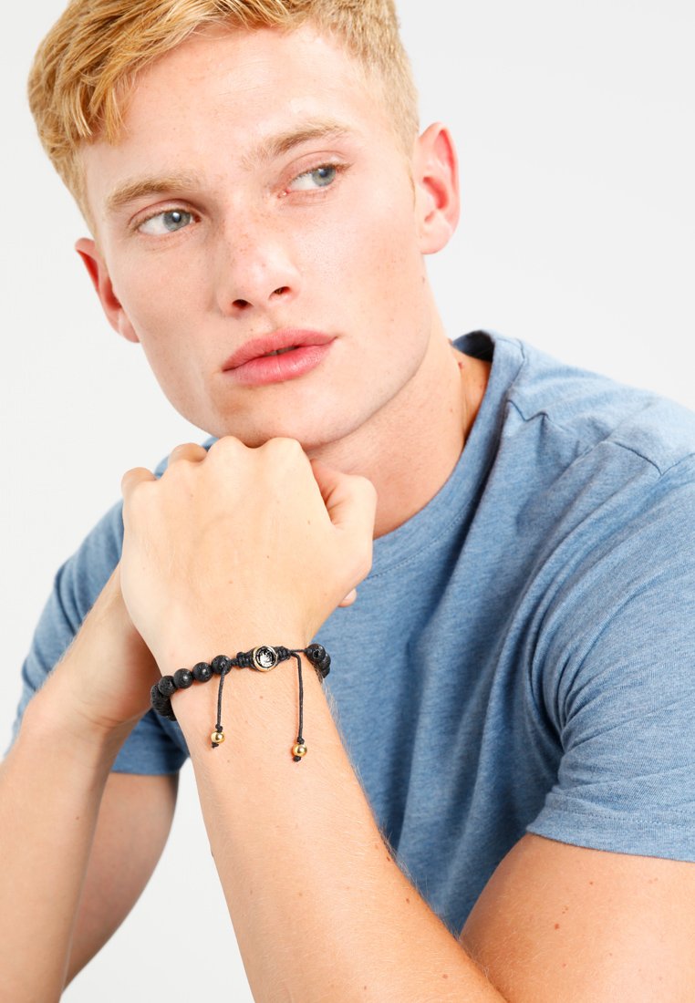 Verstellbares schwarzes Perlenarmband mit metallischen Akzenten, mit einer strukturierten Oberfläche und einem Schiebeknotenverschluss. Modell trägt es in lässiger Umgebung.