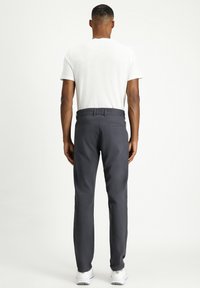 Pantalones gris oscuro con corte recto, fabricados en un tejido suave. Presentan dos bolsillos traseros y una cinturilla estándar. Se llevan con una camiseta blanca.