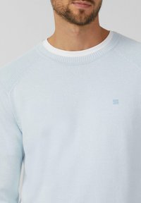 Lichtblauwe gebreide trui met een geribde ronde halslijn en schoudernaden. Het heeft een klein logo geborduurd op de borst.